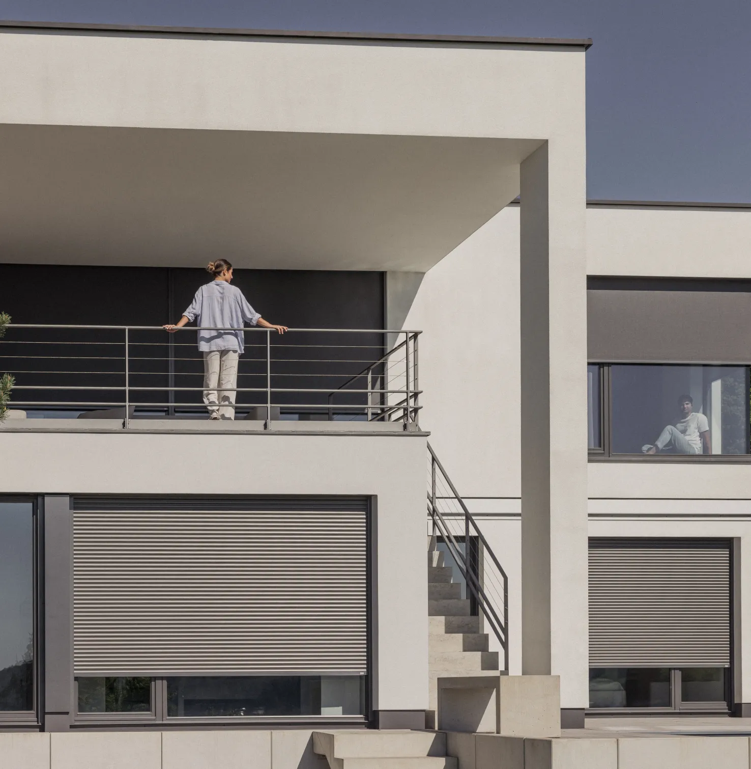Huis met rolluiken en screens van textiel met een vrouw op het balkon